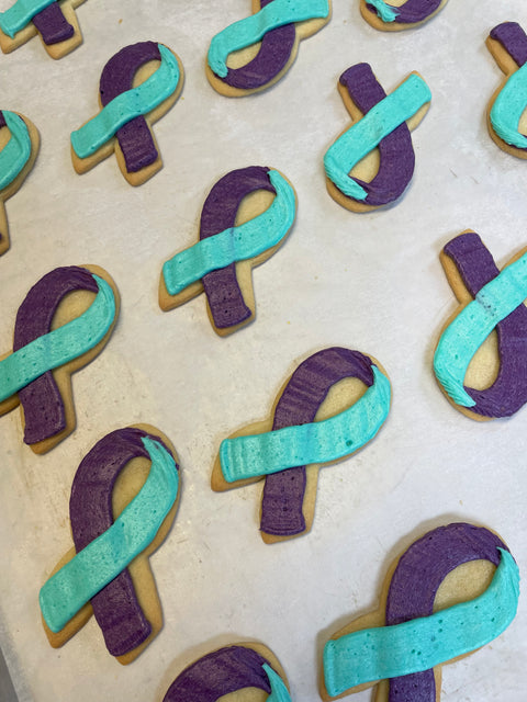 A cookie sheet filled with teal and purple ribbon-shaped buttercream cookies