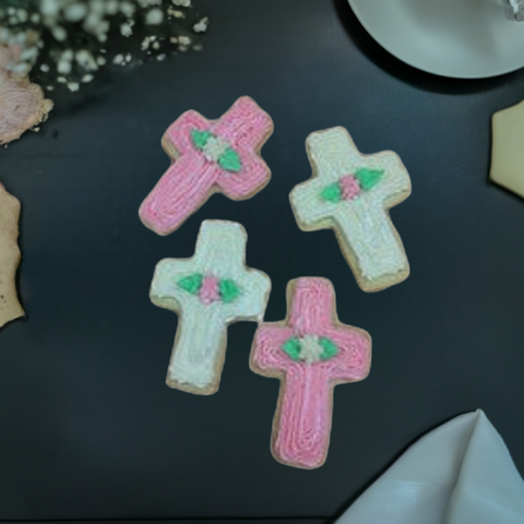 Hand reaching for a pink cross cookie on a blue background, decorated with white frosting, beside a cup of coffee.