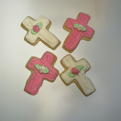 cross cut out sugar cookie on a white background, decorated with white and pink buttercream frosting with flowers.